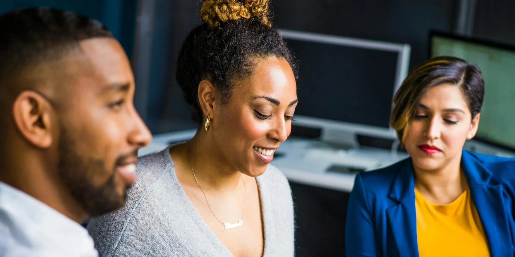 Three people engaged in a conversation in a professional setting, appearing focused and collaborative.