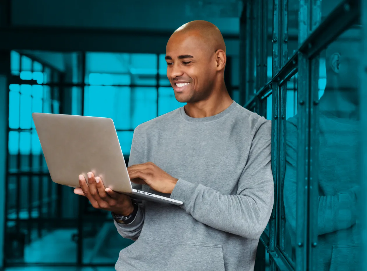 Man standing and smiling while working on a laptop.