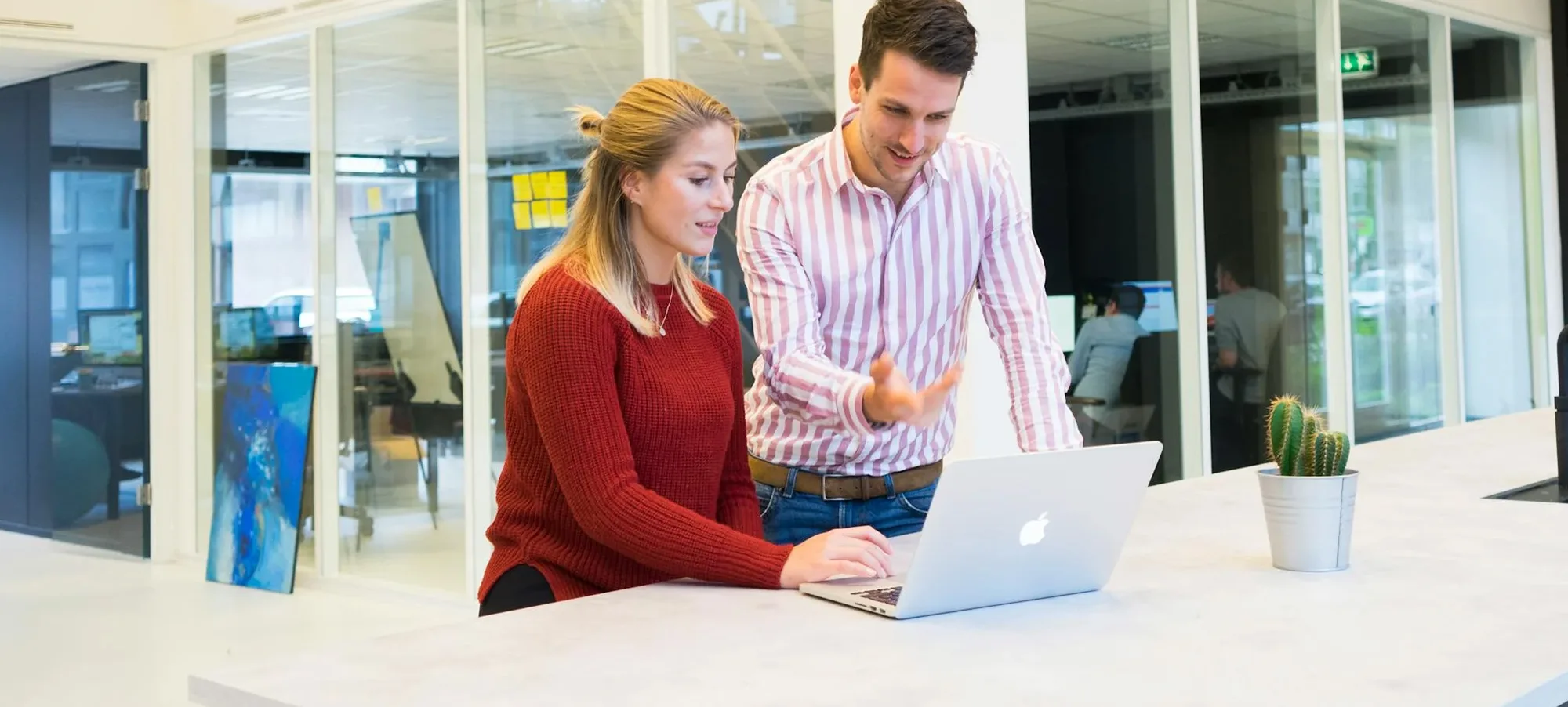 Two people standing in an office, discussing something with a laptop in hand.