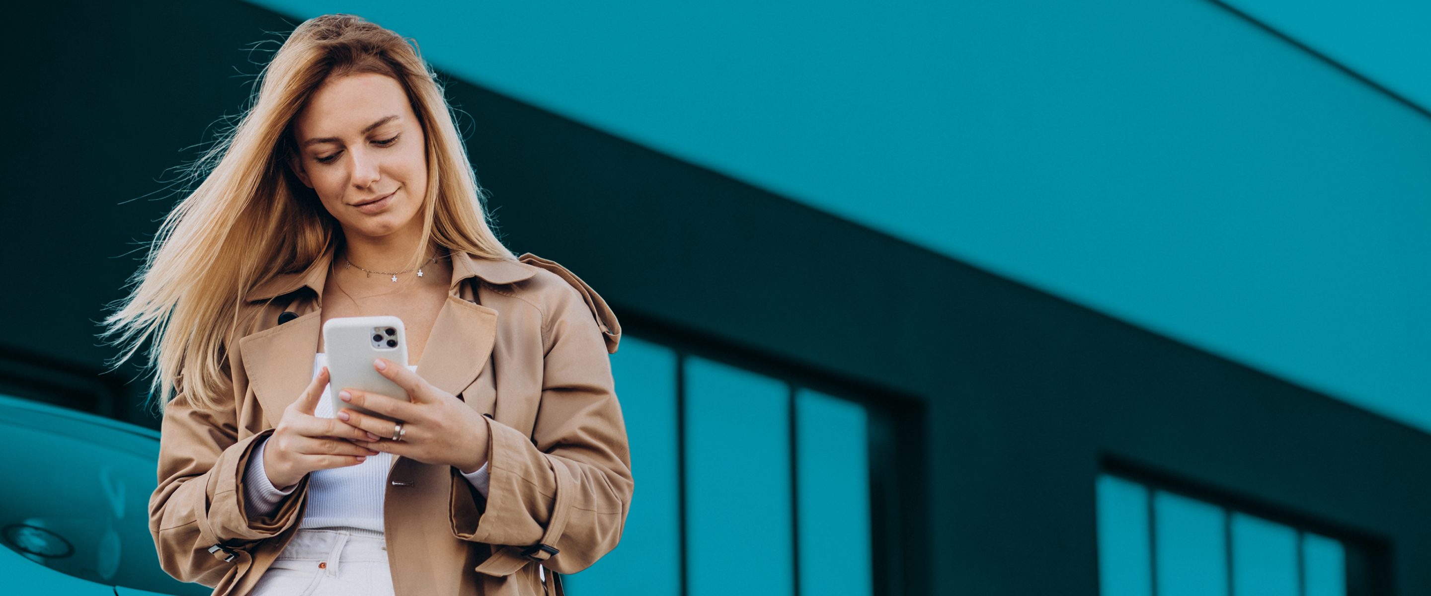 Woman standing in a parking lot, using her phone while the wind blows her hair.