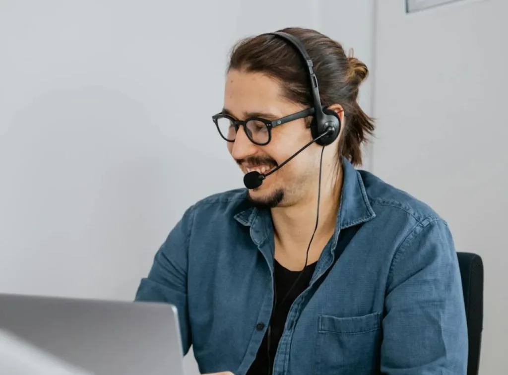 Person in a customer support role wearing a headset, smiling while working on a laptop.