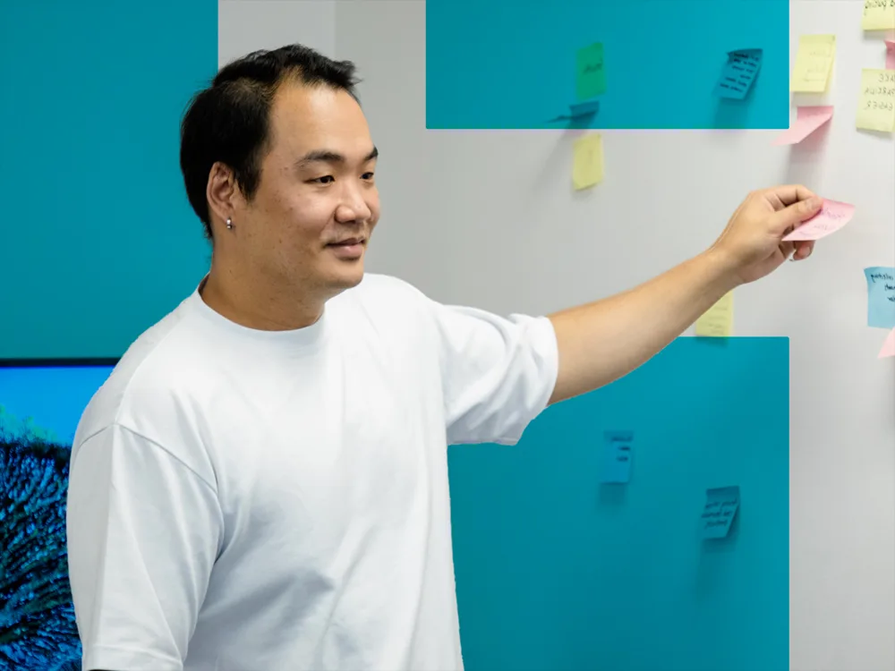 A man stands in front of a wall covered with sticky notes, placing or adjusting one.