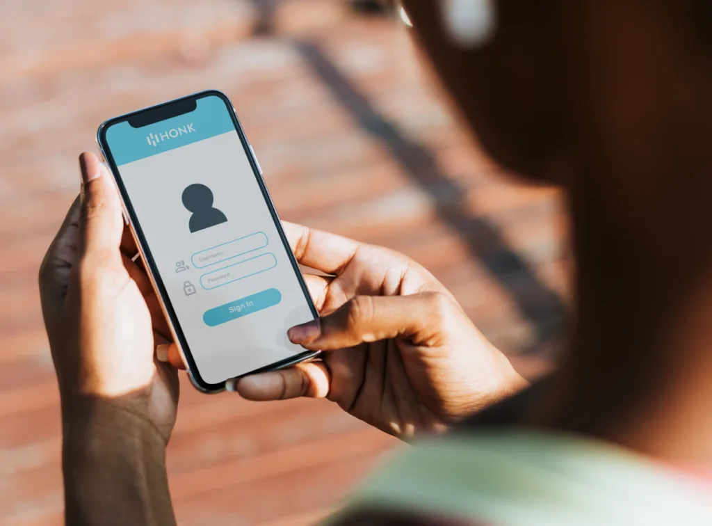 A person holding a smartphone displaying a login screen, with fields for a username and password.