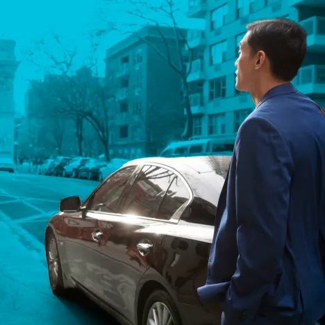 A man in a blue jacket is standing on a city street, looking at a parked car.