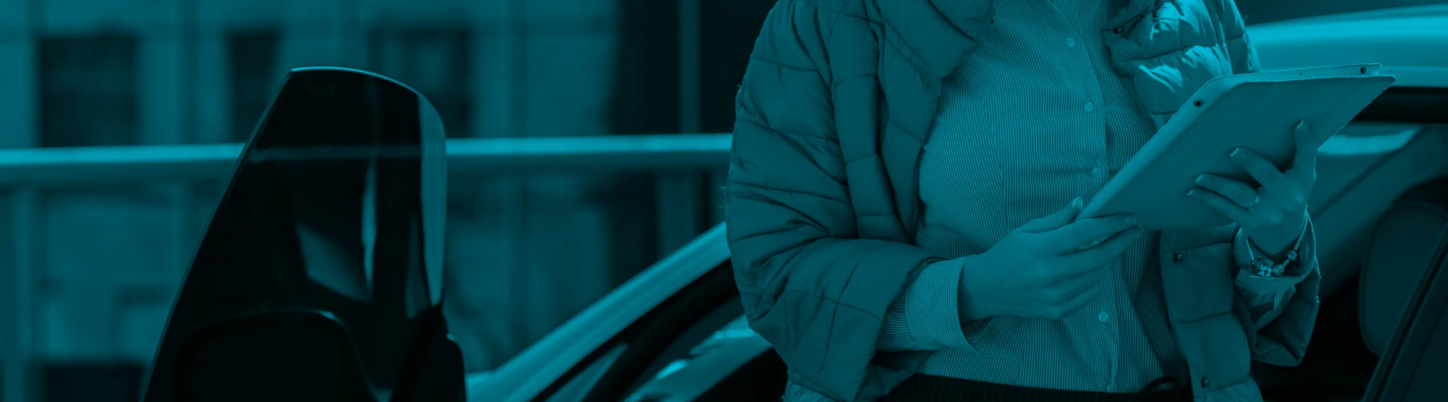 A person holding a tablet stands near a car.