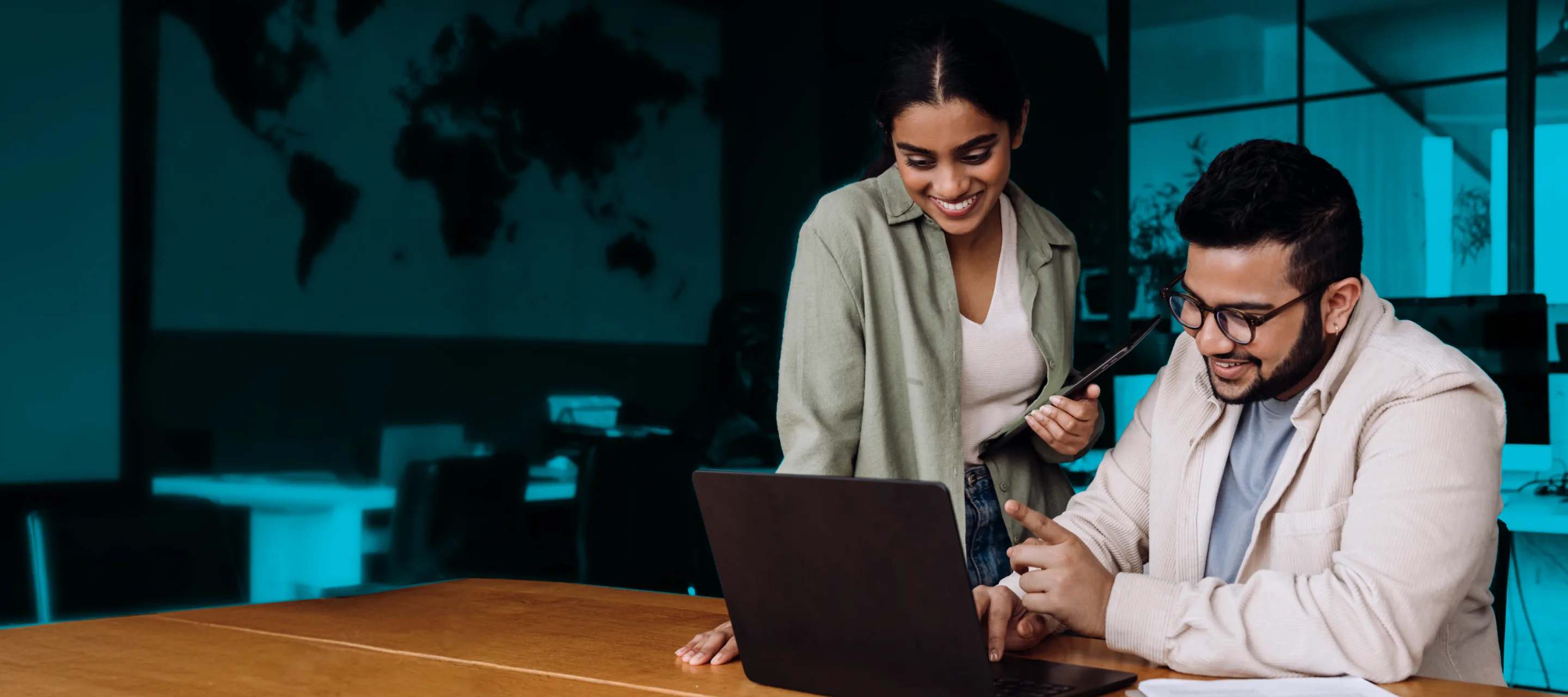 A man and woman are smiling and collaborating while looking at a laptop.